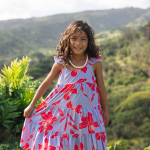 little girl with brown hair wearing a mid length dress with periwinkle background and bright red hibiscus print.