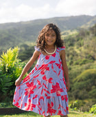 little girl with brown hair wearing a mid length dress with periwinkle background and bright red hibiscus print.