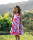 little girl with brown hair wearing a mid length dress with periwinkle background and bright red hibiscus print.