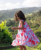 little girl with brown hair wearing a mid length dress with periwinkle background and bright red hibiscus print.