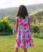 little girl with brown hair wearing a mid length dress with periwinkle background and bright red hibiscus print.
