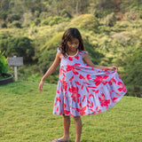 little girl with brown hair wearing a mid length dress with periwinkle background and bright red hibiscus print.