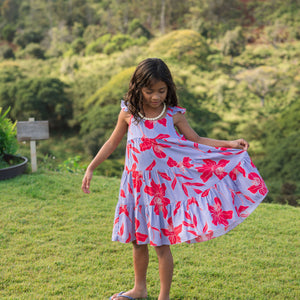 little girl with brown hair wearing a mid length dress with periwinkle background and bright red hibiscus print.
