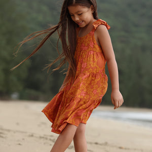 little girl wearing an orange flowy dress with puakenikeni print