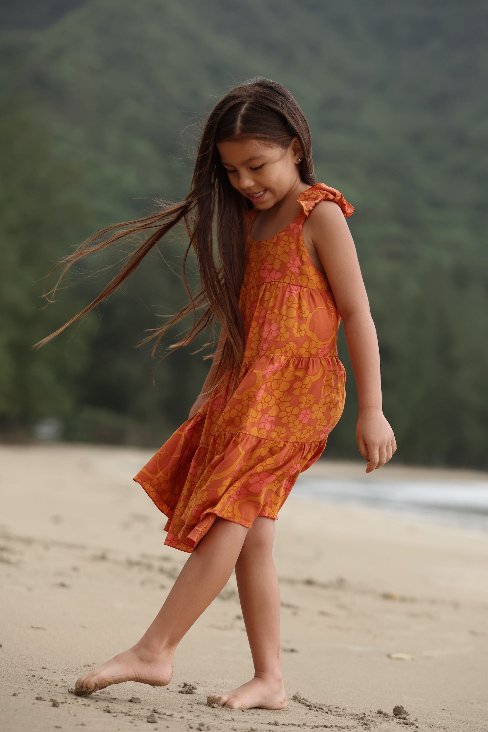 little girl wearing an orange flowy dress with puakenikeni print