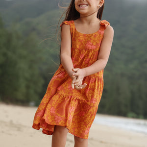 little girl wearing an orange flowy dress with puakenikeni print