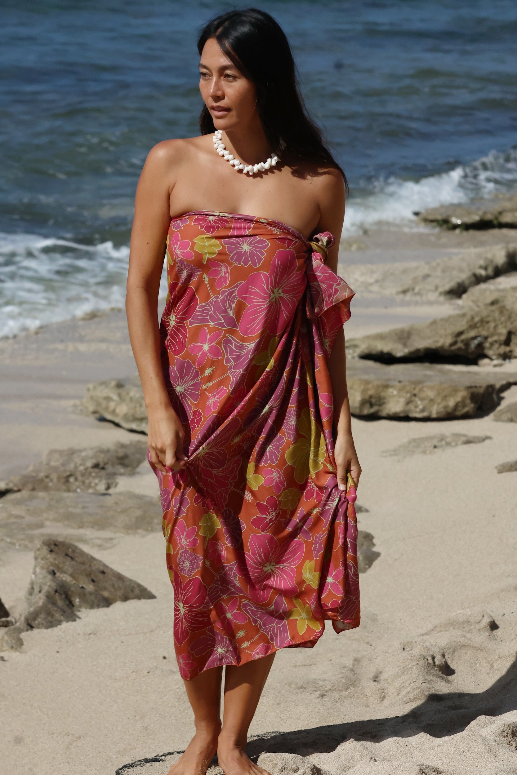 woman with brown hair wearing terracotta colored pareo with large purple and yellow flower print