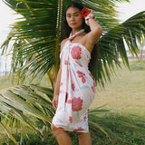 woman with brown hair wearing light white pinkish pareo with large red hibiscus print