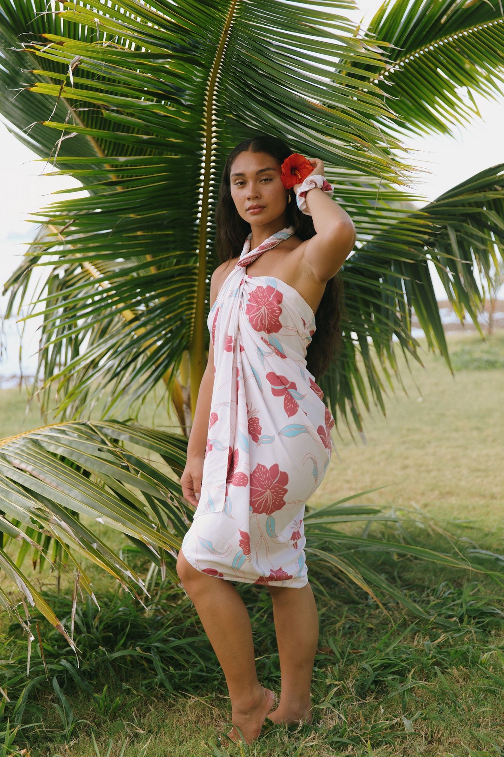 woman with brown hair wearing light white pinkish pareo with large red hibiscus print