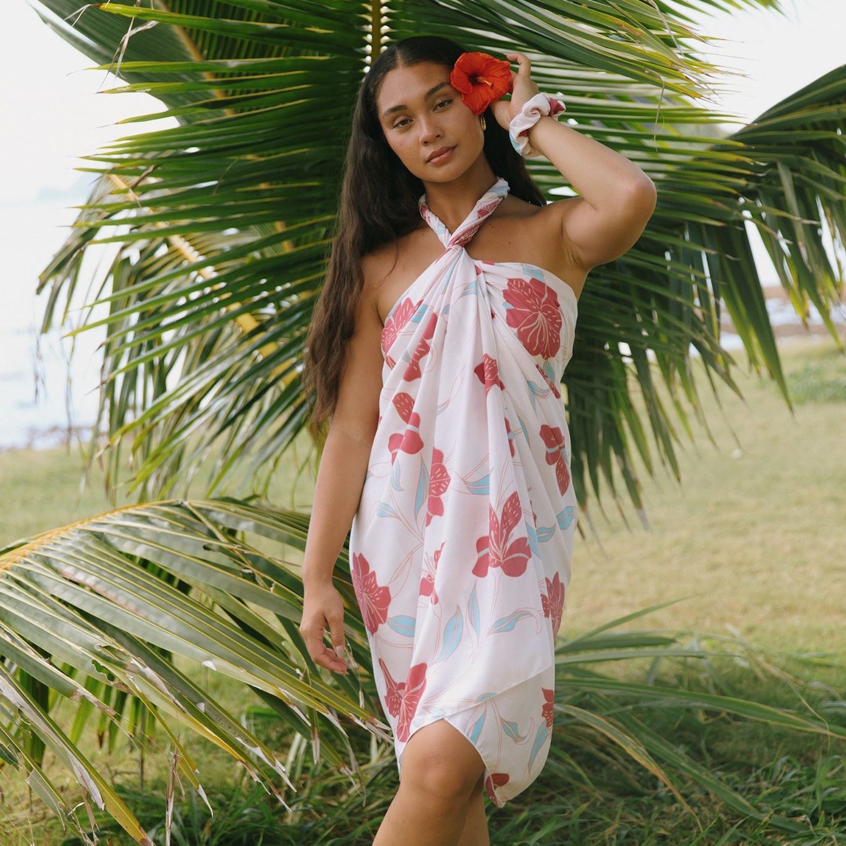 woman with brown hair wearing light white pinkish pareo with large red hibiscus print
