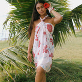 woman with brown hair wearing light white pinkish pareo with large red hibiscus print