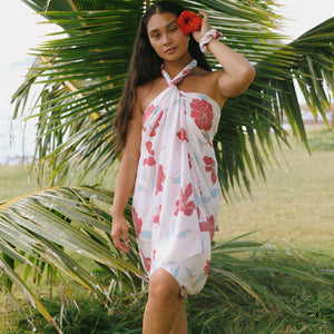 woman with brown hair wearing light white pinkish pareo with large red hibiscus print