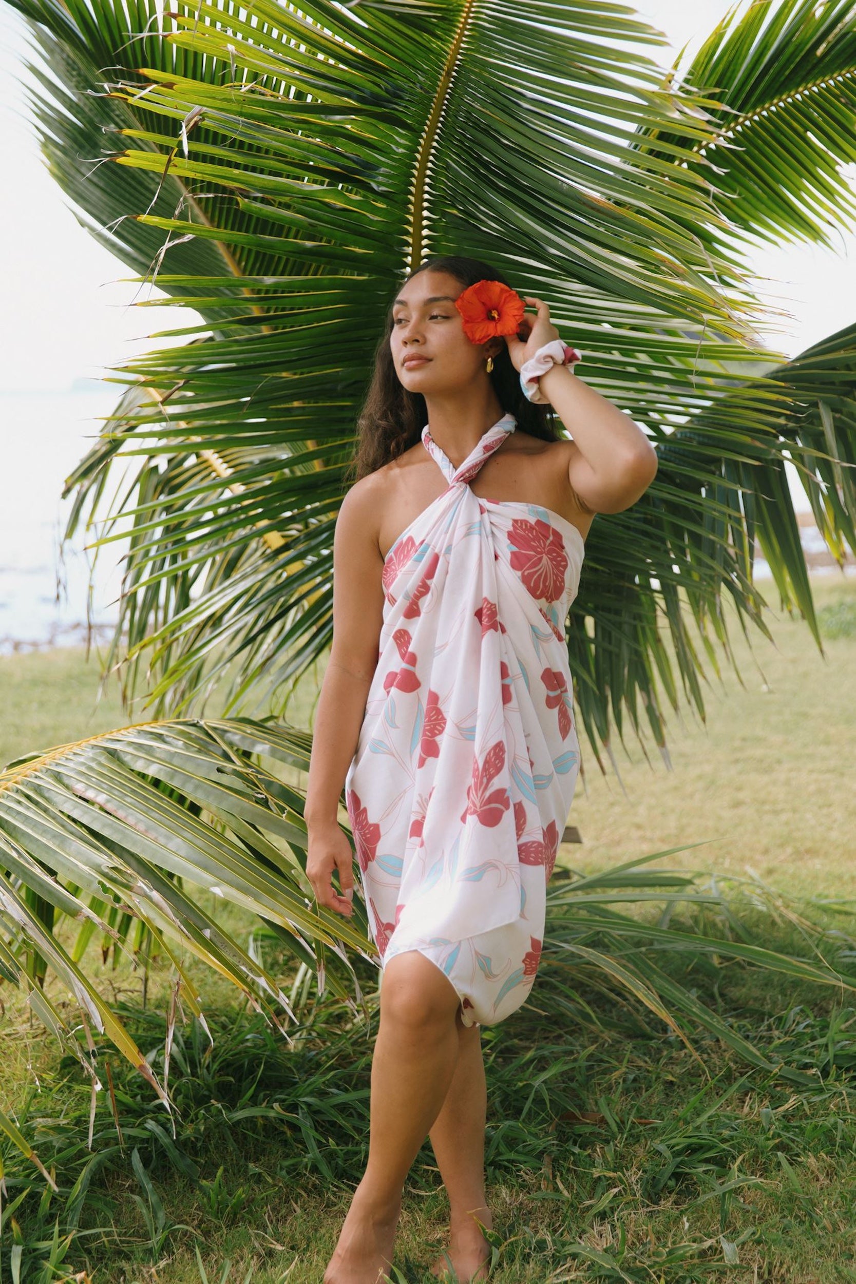 woman with brown hair wearing light white pinkish pareo with large red hibiscus print