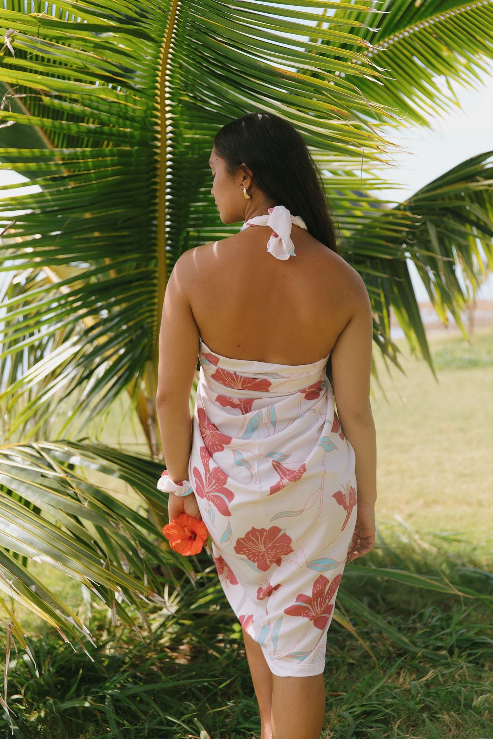 woman with brown hair wearing light white pinkish pareo with large red hibiscus print
