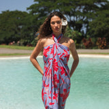 woman with brown hair wearing a pareo with periwinkle background and bright red hibiscus print.