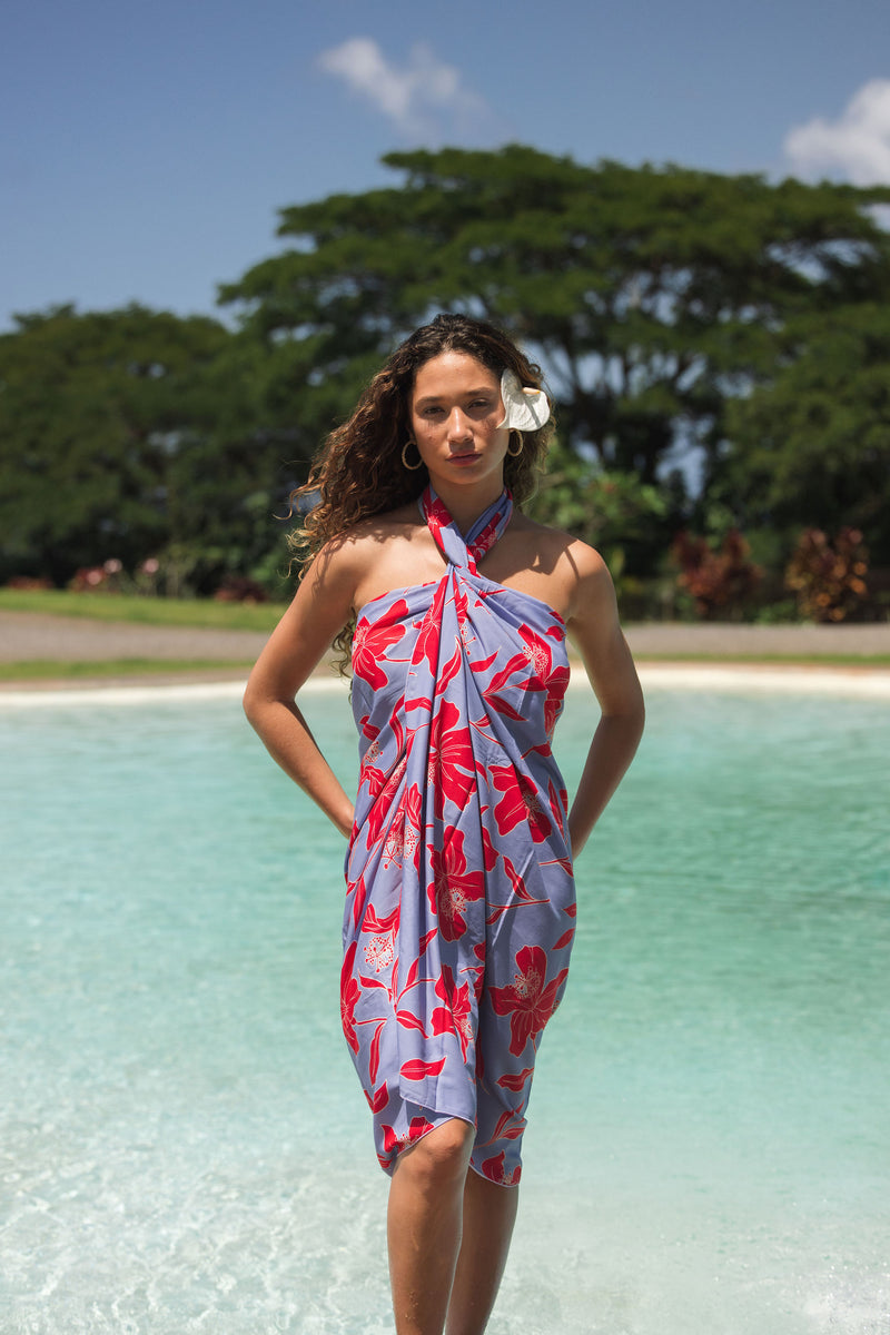woman with brown hair wearing a pareo with periwinkle background and bright red hibiscus print.