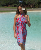 woman with brown hair wearing a pareo with periwinkle background and bright red hibiscus print.