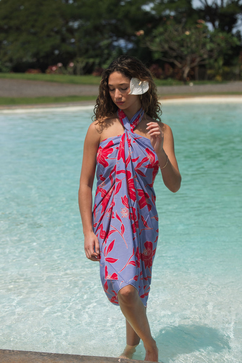woman with brown hair wearing a pareo with periwinkle background and bright red hibiscus print.