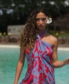 woman with brown hair wearing a pareo with periwinkle background and bright red hibiscus print.