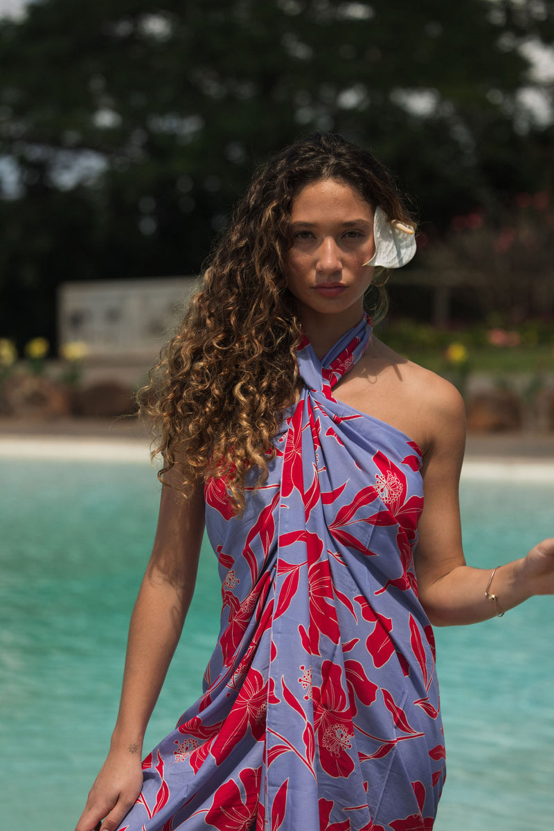 woman with brown hair wearing a pareo with periwinkle background and bright red hibiscus print.