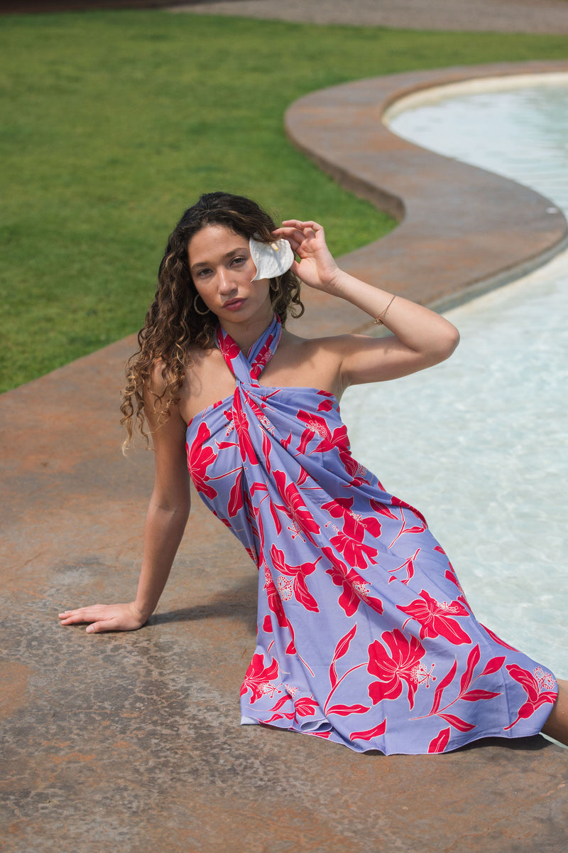 woman with brown hair wearing a pareo with periwinkle background and bright red hibiscus print.
