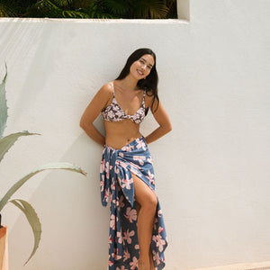 woman with black hair wearing a pareo in a navy and pink hibiscus print. 