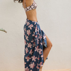 woman with black hair wearing a pareo in a navy and pink hibiscus print. 