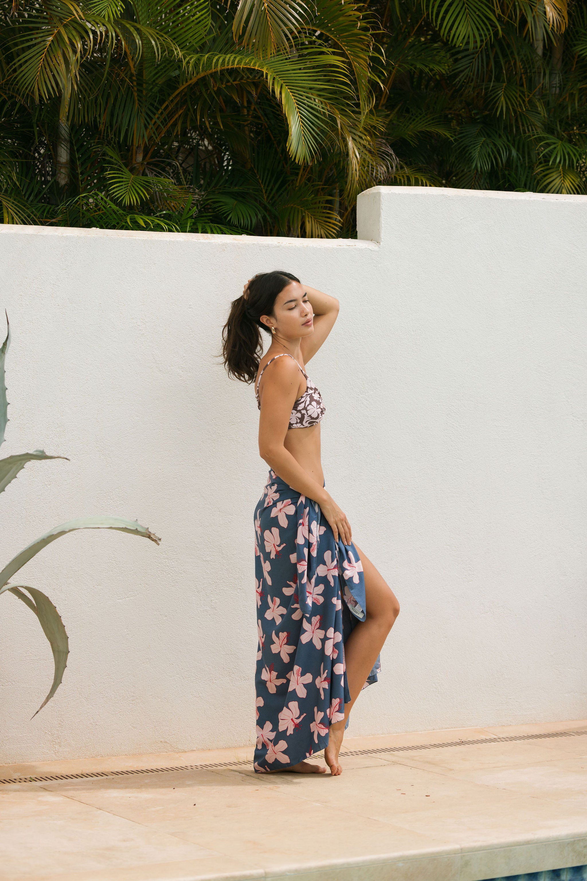 woman with black hair wearing a pareo in a navy and pink hibiscus print. 