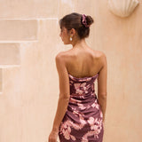 woman with brown hair wearing a brown/maroon toned pareo with pink lei awapuhi print
