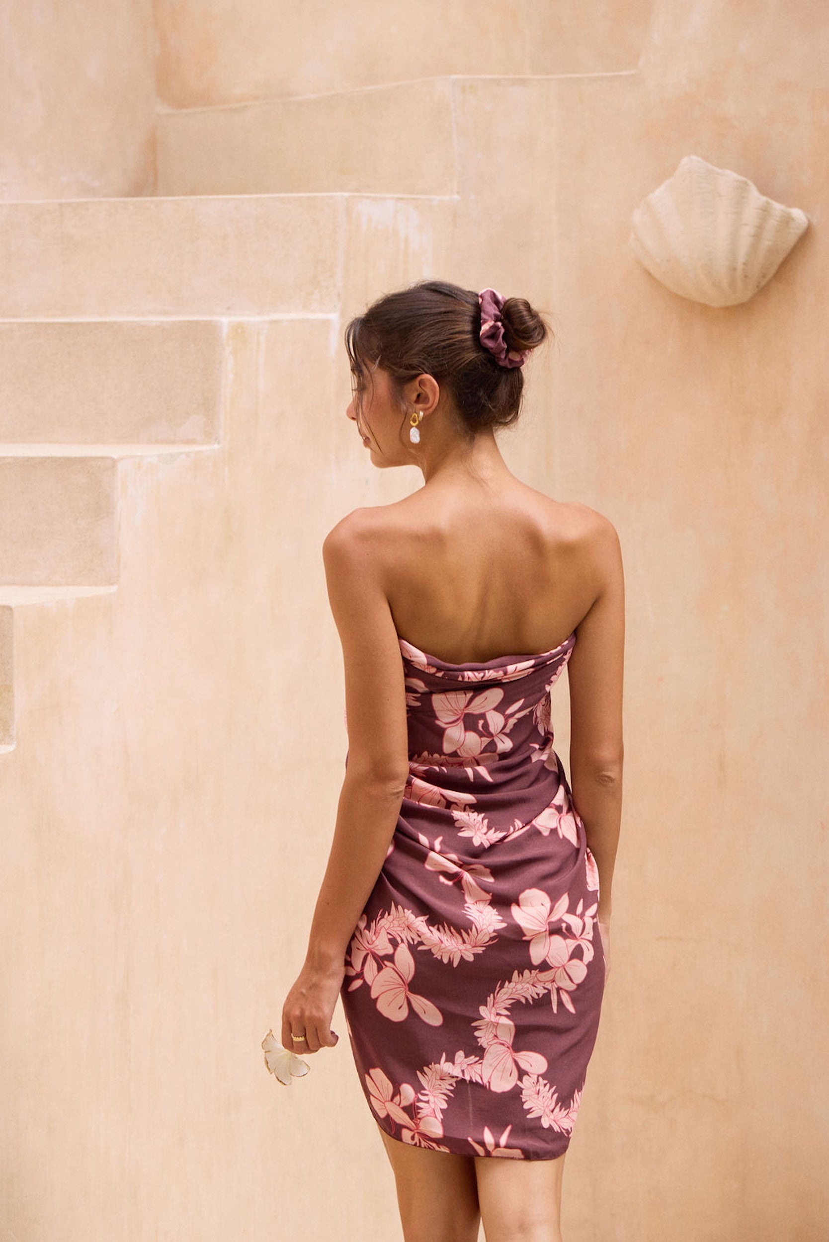 woman with brown hair wearing a brown/maroon toned pareo with pink lei awapuhi print