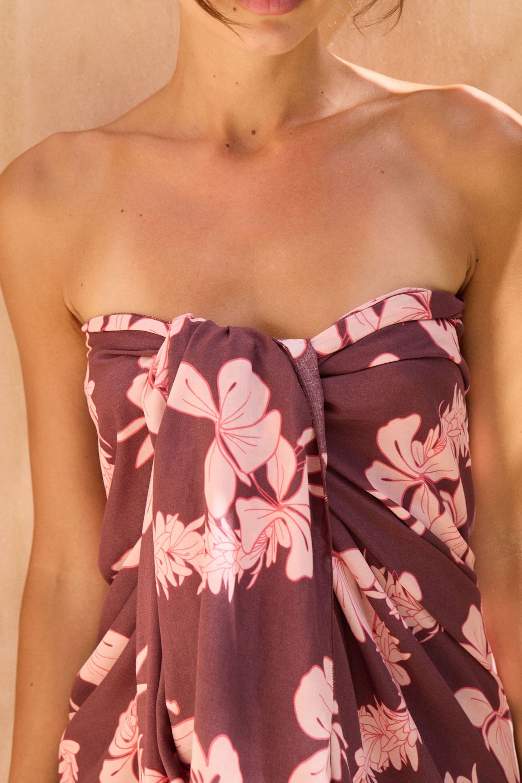 woman with brown hair wearing a brown/maroon toned pareo with pink lei awapuhi print