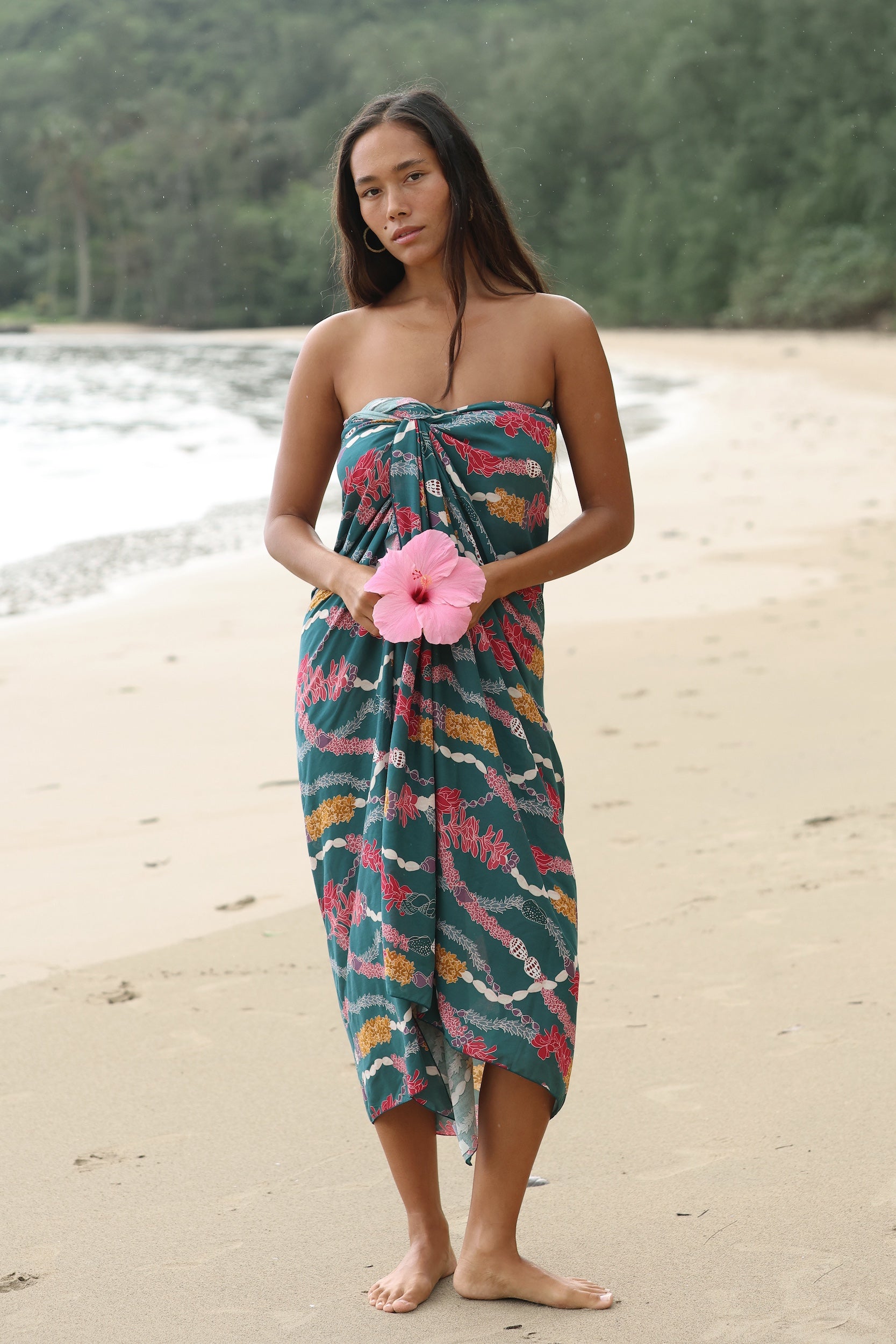 woman with brown hair wearing a dark teal pareo with shell lei print