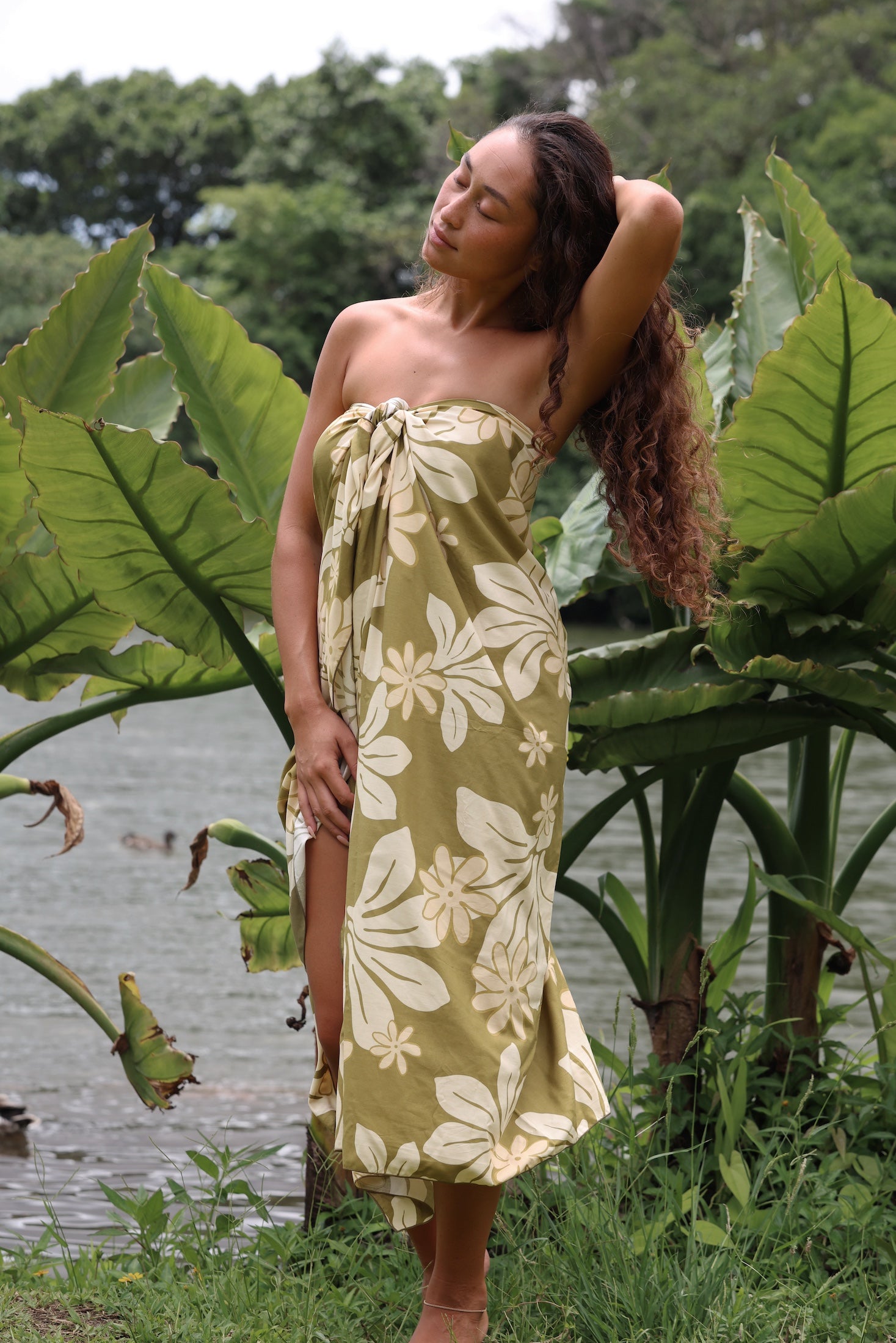 woman with brown hair wearing a pareo in a green color with naupaka pattern throughout. 