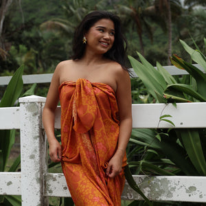 woman with brown hair wearing an orange puakenikeni pareo