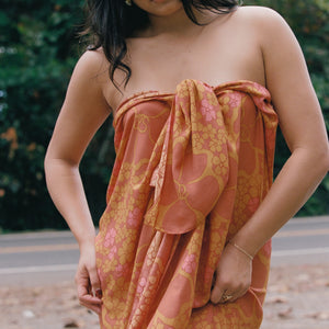 woman with brown hair wearing an orange puakenikeni pareo