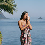 woman with brown hair wearing a teal pareo wrap with shell and pua print 