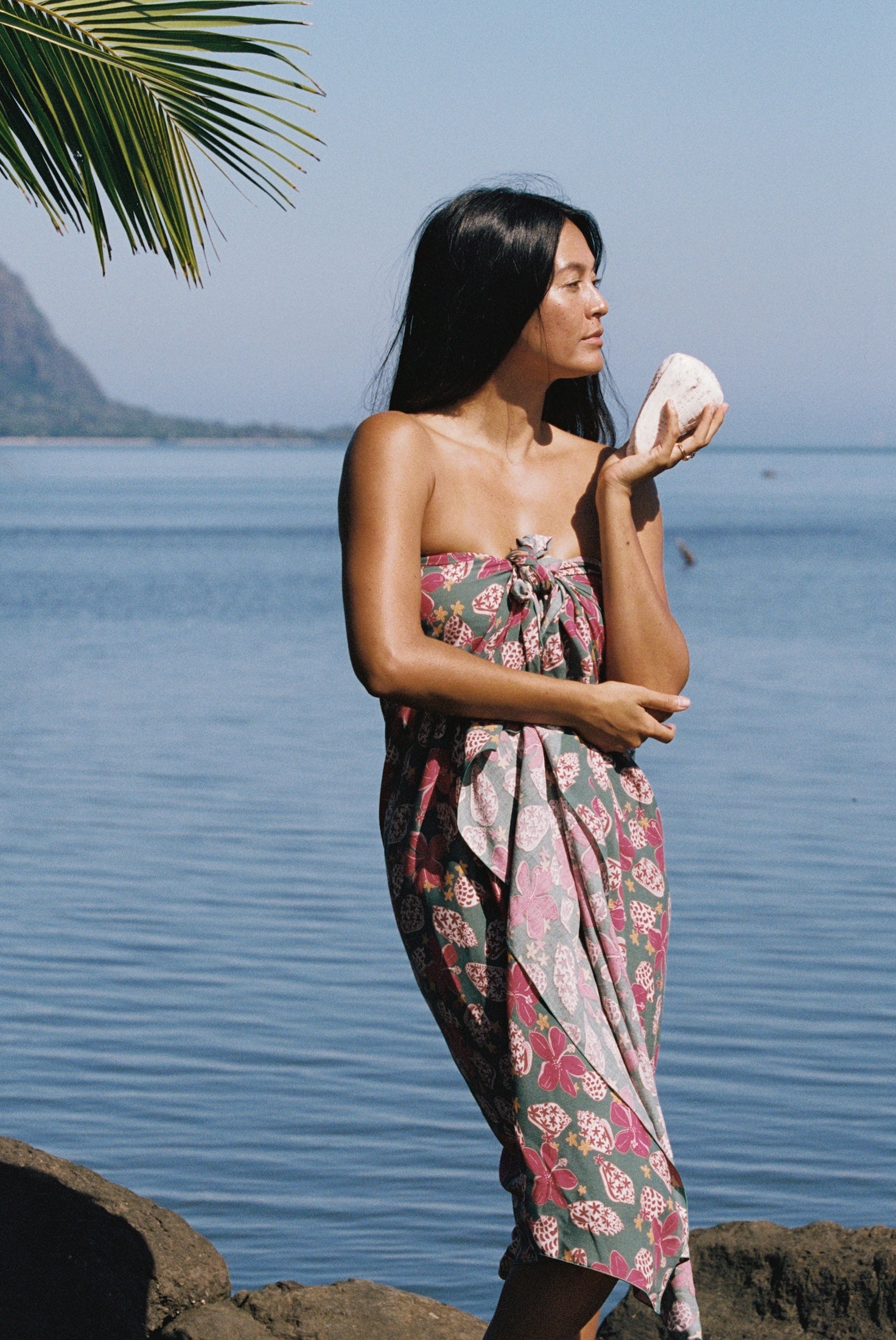 woman with brown hair wearing a teal pareo wrap with shell and pua print 