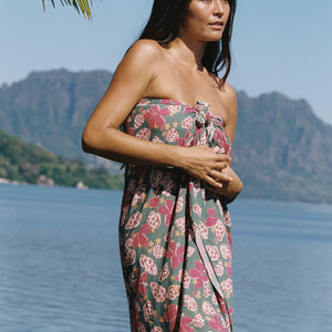 woman with brown hair wearing a teal pareo wrap with shell and pua print 