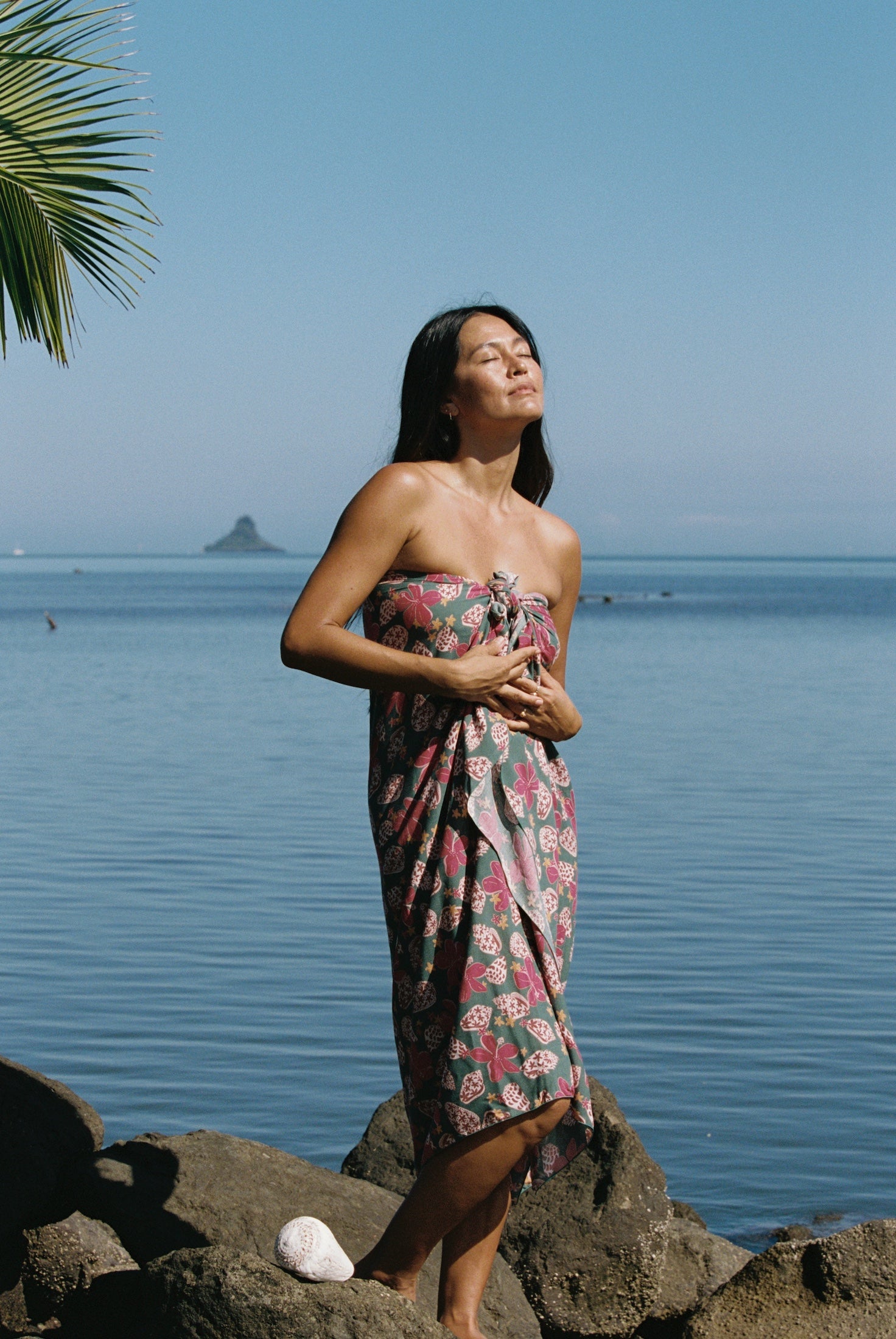 woman with brown hair wearing a teal pareo wrap with shell and pua print 