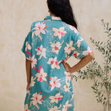  woman with brown hair wearing collared button up dress in teal with large cream colored orchids.