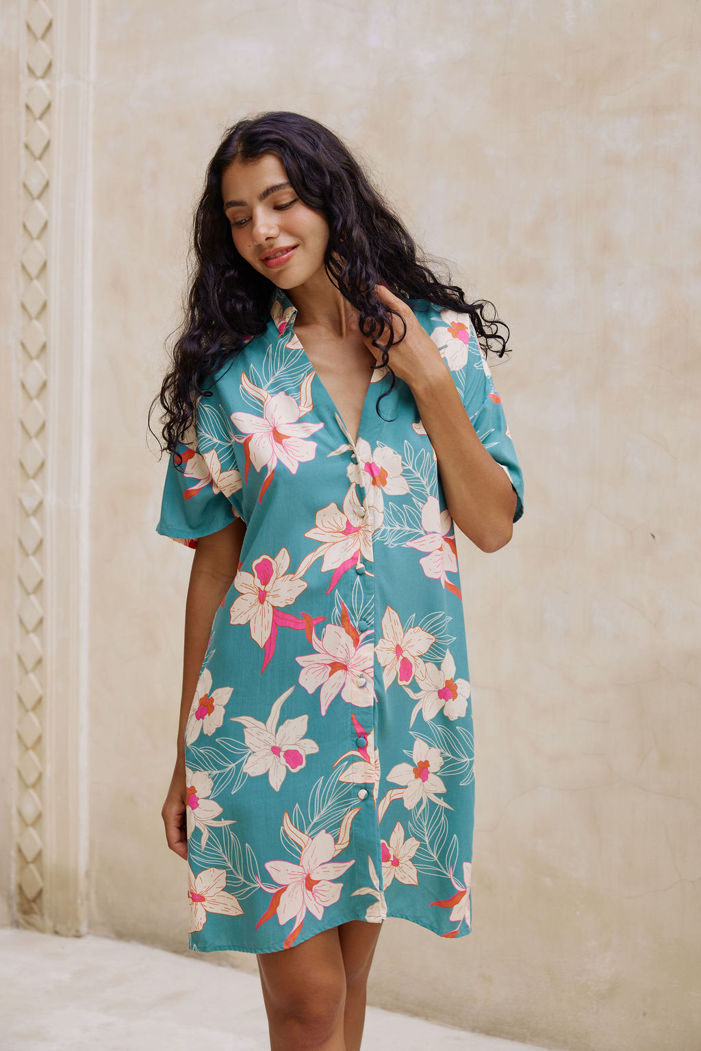 woman with brown hair wearing collared button up dress in teal with large cream colored orchids.