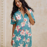 woman with brown hair wearing collared button up dress in teal with large cream colored orchids.