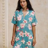 woman with brown hair wearing collared button up dress in teal with large cream colored orchids.