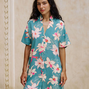 woman with brown hair wearing collared button up dress in teal with large cream colored orchids.