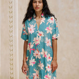 woman with brown hair wearing collared button up dress in teal with large cream colored orchids.