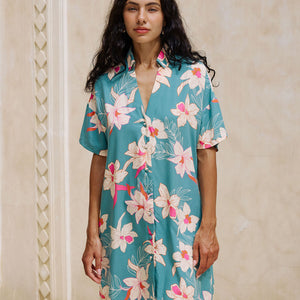 woman with brown hair wearing collared button up dress in teal with large cream colored orchids.