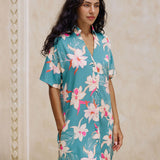 woman with brown hair wearing collared button up dress in teal with large cream colored orchids.