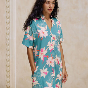 woman with brown hair wearing collared button up dress in teal with large cream colored orchids.