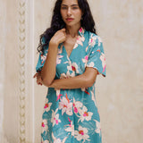 woman with brown hair wearing collared button up dress in teal with large cream colored orchids.