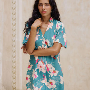 woman with brown hair wearing collared button up dress in teal with large cream colored orchids.